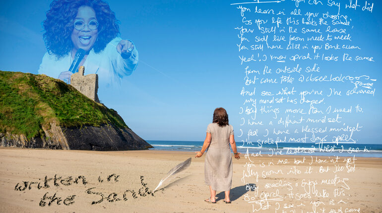 Blue Sky. A woman stands on a beach, we can see the back if her head. We see the side of a cliff. The image has text on it. The text is handwritten, like note in a scrap book. Oprah is in the sky, her image is faint. Oprah is pointing at the woman on the beach. We see the edge of a cliff. This is where Oprah is appearing above to the right of the screen.