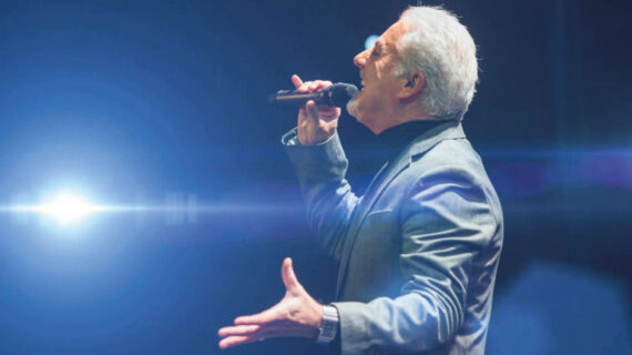 Tom Jones Tribute act on stage singing. A bright light shines towards the camera
